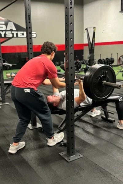 Man performing bench press with coach